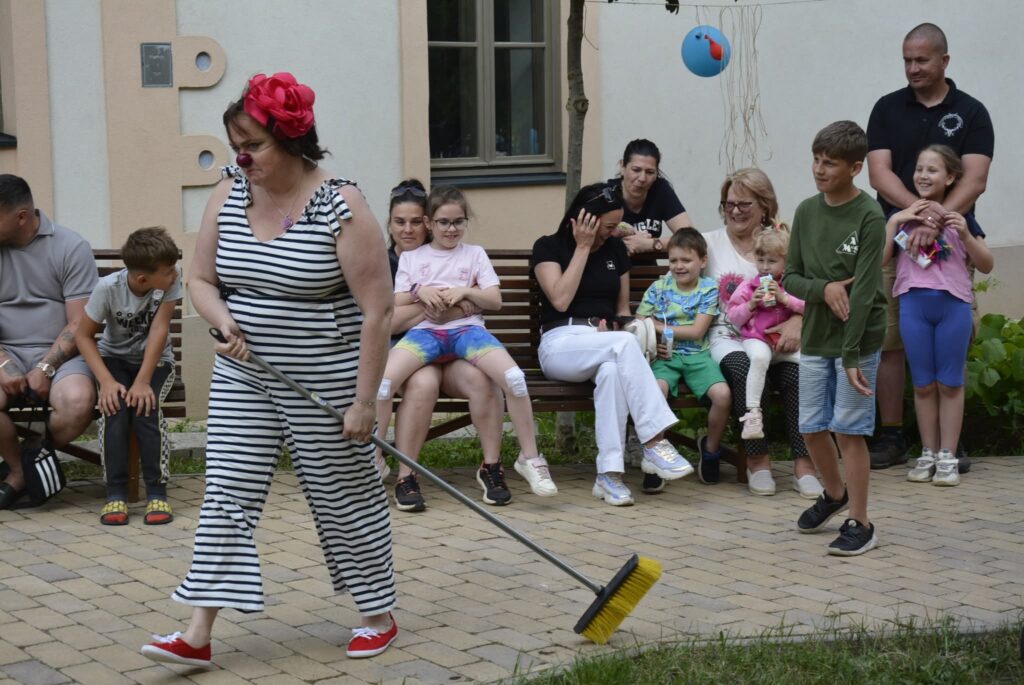 Csíkos ruhás Bohóc Angol oktató zsonglőrködik a fűben ülő gyerekek és szülők előtt